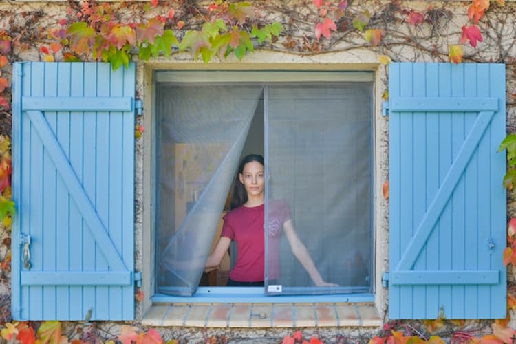 Femme se tenant devant une moustiquaire ajustable pour fenêtre Tranquilisafe